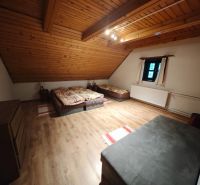 Pokoj se třemi postelemi, podlahou s dřevěným dekorem a šikmým dřevěným stropem v chatě.