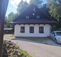 Chata ve Španí Dolině s bílou fasádou a satelitní anténou, obklopená zelení.