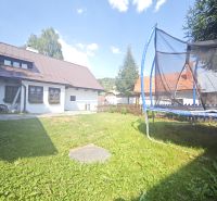 Chata ve Španělé Dolině s trampolínou na travnaté zahradě pod modrou oblohou.