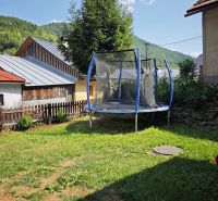 Trampolína u chaty ve Španej Dolině, obklopená trávou a stromy v pozadí.