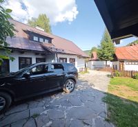 Auto zaparkované u chaty ve Španí Dolině, s viditelnými střechami a plotem.