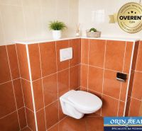 Koupelna s oranžovými obklady a závěsným WC v 1-pokojovém bytě.