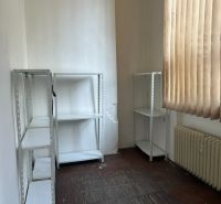 Kancelář s regály, radiátorem a závěsy, podlaha s dřevěným dekorem.