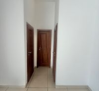 Bílé stěny s dřevěnými dveřmi a dlážděnou podlahou v obchodních prostorách.