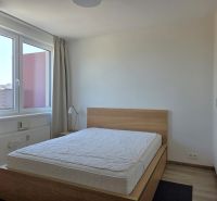Ložnice v 2-pokojovém bytě s postelí a velkým oknem, podlaha s dřevěným dekorem.