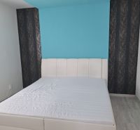 Světlá ložnice s bílou postelí a modrou stěnou v třípokojovém bytě.