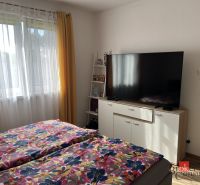 Ložnice v rodinném domě s TV, květinové povlečení, žluté závěsy, okno.