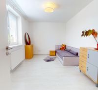 Pokoj v 3-pokojovém bytě s pohovkou, komodou a podlahou s dřevěným dekorem.