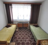 Ložnice se dvěma jednolůžky, kobercem a oknem v 2-pokojovém bytě.