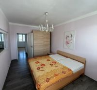 Ložnice v 3-pokojovém bytě s postelí, lustrem a podlahou s dřevěným dekorem.
