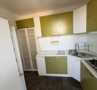 Kuchyně ve 3-pokojovém bytě s podlahou s dřevěným dekorem, zelenými a bílými skříňkami.