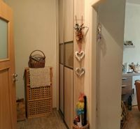 V 2-pokojovém bytě je dřevěný dekor, košík, dekorace a výhled na kuchyň.