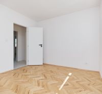 Pokoj s bílými stěnami, podlahou s dřevěným dekorem ve 3-pokojovém bytě.