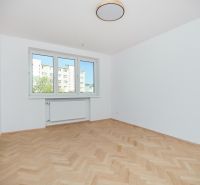 Pokoj v 3-pokojovém bytě s bílými stěnami a podlahou s dřevěným dekorem.