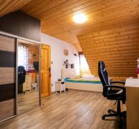 Podkrovní pokoj s dřevěným obkladem stropu, postelí, skříní a podlahou s dřevěným dekorem.