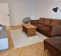 Obývací pokoj v 2-pokojovém bytě, hnědá sedačka, konferenční stolek, podlaha s dřevěným dekorem.