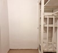 Úložný prostor s bílými poličkami v 2-pokojovém bytě, s podlahou pokrytou kobercem.