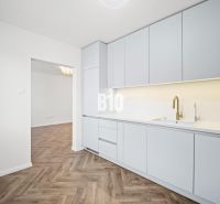 Kuchyně ve 3-pokojovém bytě s bílým nábytkem a podlahou s dřevěným dekorem.