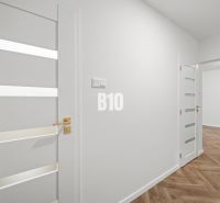 Bílý interiér 3pokojového bytu s podlahou s dřevěným dekorem a elegantními dveřmi.
