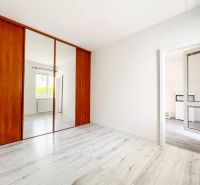 Čistý bílý interiér s velkou zrcadlovou skříní a podlahou s dřevěným dekorem v 2-pokojovém bytě.