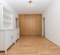 Chodba v 3-pokojovém bytě s bílou skříňkou a podlahou s dřevěným dekorem.