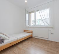 Jednolůžková postel a okno s bílými závěsy ve 3-pokojovém bytě na podlaze s dřevěným dekorem.