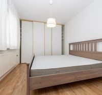 Ložnice ve 3pokojovém bytě s dřevěnou postelí a podlahou s dřevěným dekorem.