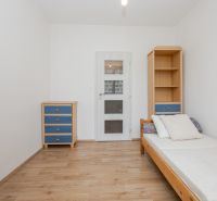 Jednoduchý pokoj s postelí, skříňkou a podlahou s dřevěným dekorem ve 3-pokojovém bytě.