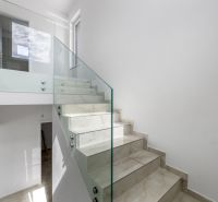 Skleněné zábradlí se schodištěm v rodinném domě, světlá místnost, jednoduchý design.