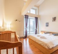Světlá ložnice v rekreačním apartmánu s dětskou postýlkou a podlahou s dřevěným dekorem.