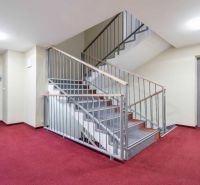 Chodba v rekreačním apartmánu s červeným kobercem, schodištěm a výtahem.