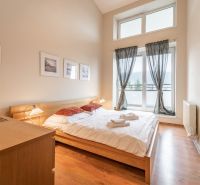 Světlá ložnice s manželskou postelí a podlahou s dřevěným dekorem v rekreačním apartmánu.