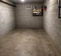 Prázdná garáž s policí na nářadí a osvětlením, betonová podlaha.
