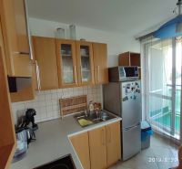 Kuchyně s dřevěnými skříňkami, mikrovlnkou a lednicí v 2-pokojovém bytě.