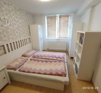 Ložnice s postelí, podlahou s dřevěným dekorem a květinovou tapetou v 2-pokojovém bytě.