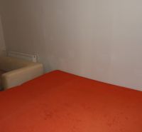 Pokoj s oranžovou postelí a béžovým křeslem v dvoupokojovém bytě.