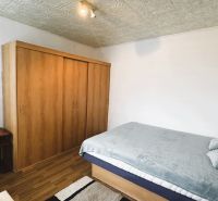 Ložnice ve 4pokojovém bytě s postelí, skříní a podlahou s dřevěným dekorem.