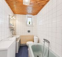 Koupelna s obklady, modrou podlahou, vanou a dřevěným stropem v rodinném domě.