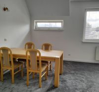 Stůl se čtyřmi židlemi v 2-pokojovém bytě, šedý koberec, dvě okna.