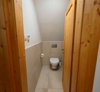 Interiér chaty s WC, světlé dlaždice a dřevěné obložení stěn dveří.