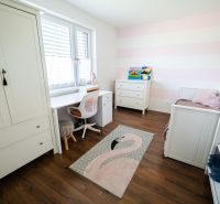 Dětský pokoj s bílým nábytkem a podlahou s dřevěným dekorem v rodinném domě.