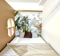 Postel se vzorovanou dekou, v 1-pokojovém bytě s tropickou tapetou a polštáři.
