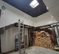 Rodinný dům s dřevěnými trámy a uskladněným dřevem v interiéru.