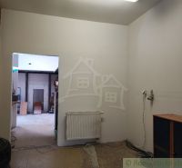 Interiér rodinného domu s bílými stěnami, radiátorem a otevřenými dveřmi.