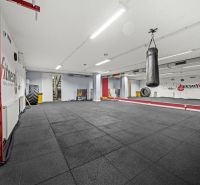 Fitness prostor s boxovacím pytlem, velkými zrcadly a černou podlahou.
