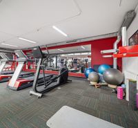 Fitness centrum s běžeckými pásy a cvičebními pomůckami v obchodních prostorách.
