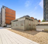 Exteriér Bratislava - Nivy, Trenčianska: Fitness centrum obklopené moderními budovami a zpevněnými plochami.