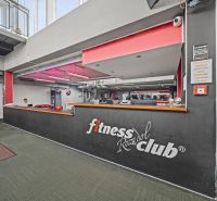 Recepce fitness klubu s nápisem, červeným osvětlením a dekorativními trofejemi na zemi zeleného odstínu.