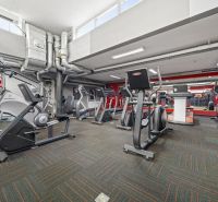 Fitness centrum s posilovacím vybavením, zrcadly a vzduchotechnikou v obchodních prostorech.