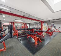 Fitness centrum s posilovacími zařízeními, lavicemi a zrcadly v obchodních prostorách.